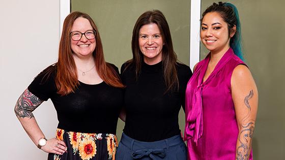 三位来自《OG官网》的女性获得了今年的游戏奖提名，她们站在一起，对着镜头微笑.