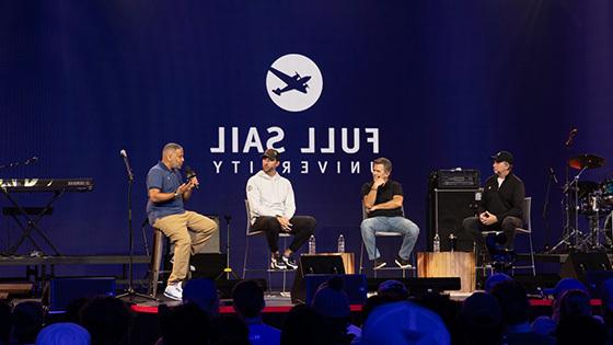 美国职业棒球大联盟投手亚当·温赖特和其他三个人坐在一个小组讨论的舞台上, 他们身后的大型LED屏幕在蓝色背景下写着“Full Sail University”.