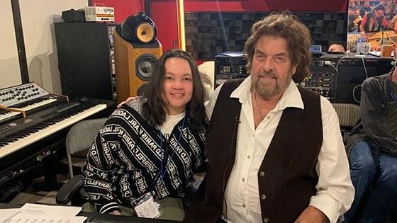 Alan Parsons sits with Steffie Tjandra in front of a mixing board in a recording studio. 他们对着镜头微笑.
