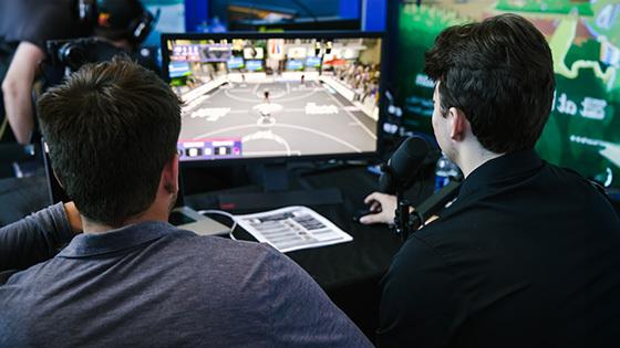 两个人背对着镜头，在他们面前桌子上的一个小显示器上观看“NBA 2K”游戏.