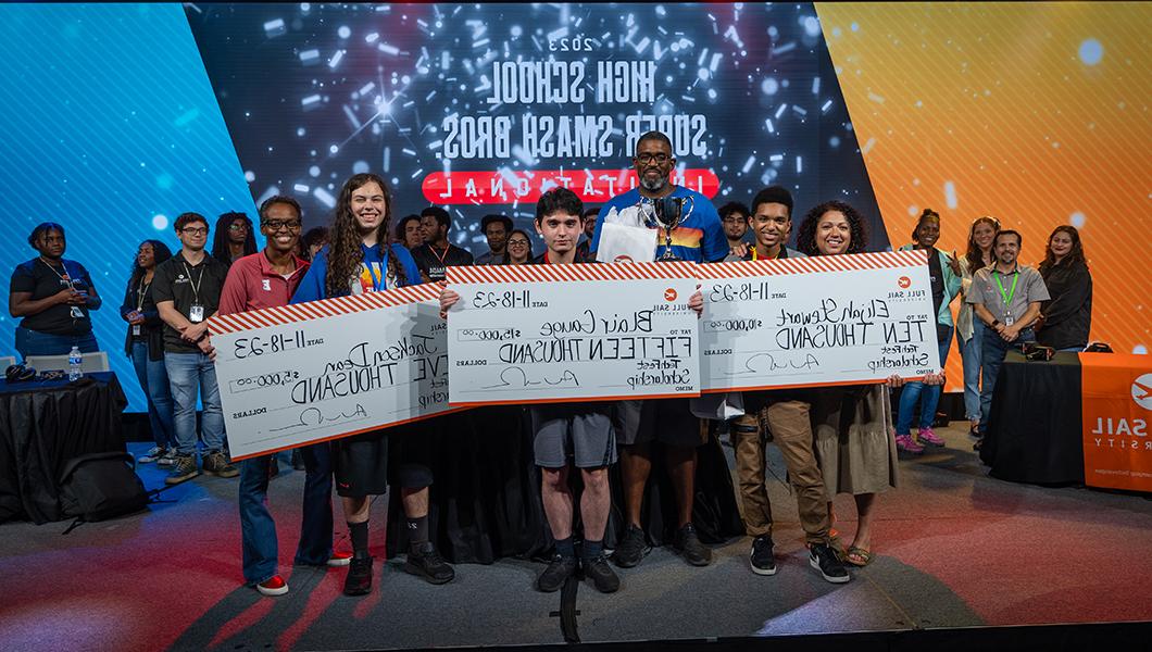 Three young people are seen on stage holding large novelty checks with scholarship funds from Full Sail.
